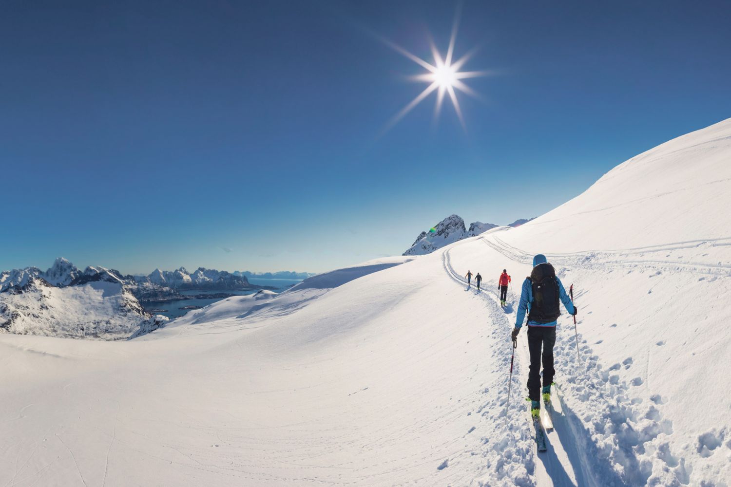 Mehrere Personen machen bei blauem Himmel einen Langlauf im Schnee in den Bergen. 